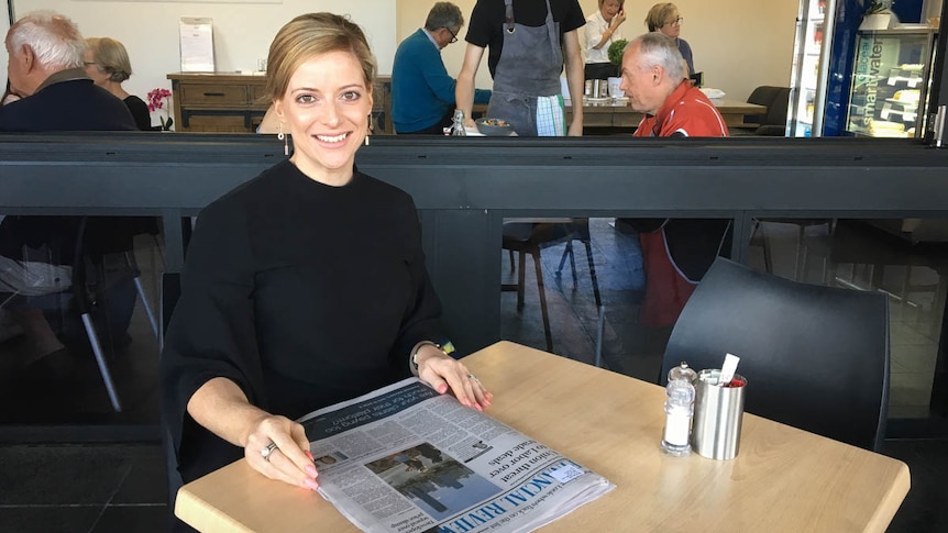 Woman sitting at cafe table with newspaper