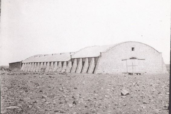 A long stone shed with a curved roof stands in an open plain of gibber rock with a double wooden door on the front