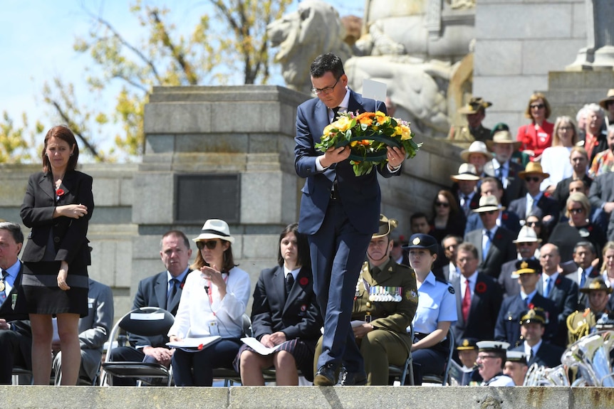 a man walks down steps at a memorial to lay a wreath of flowers
