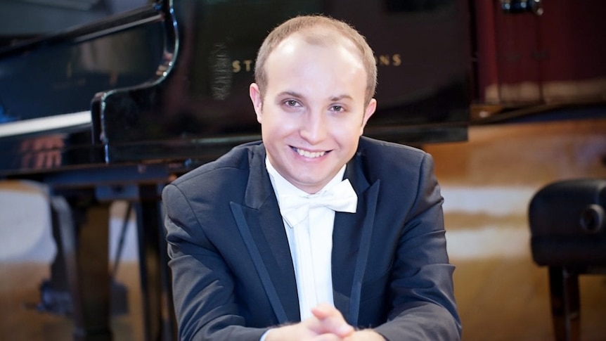 Pianist Alexander Gavrylyuk sitting on stage with a grand piano behind him
