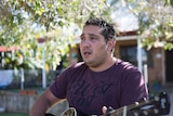 An Indigenous man singing and playing the guitar