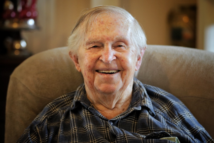 An old man sitting in an armchair smiling at the camera.