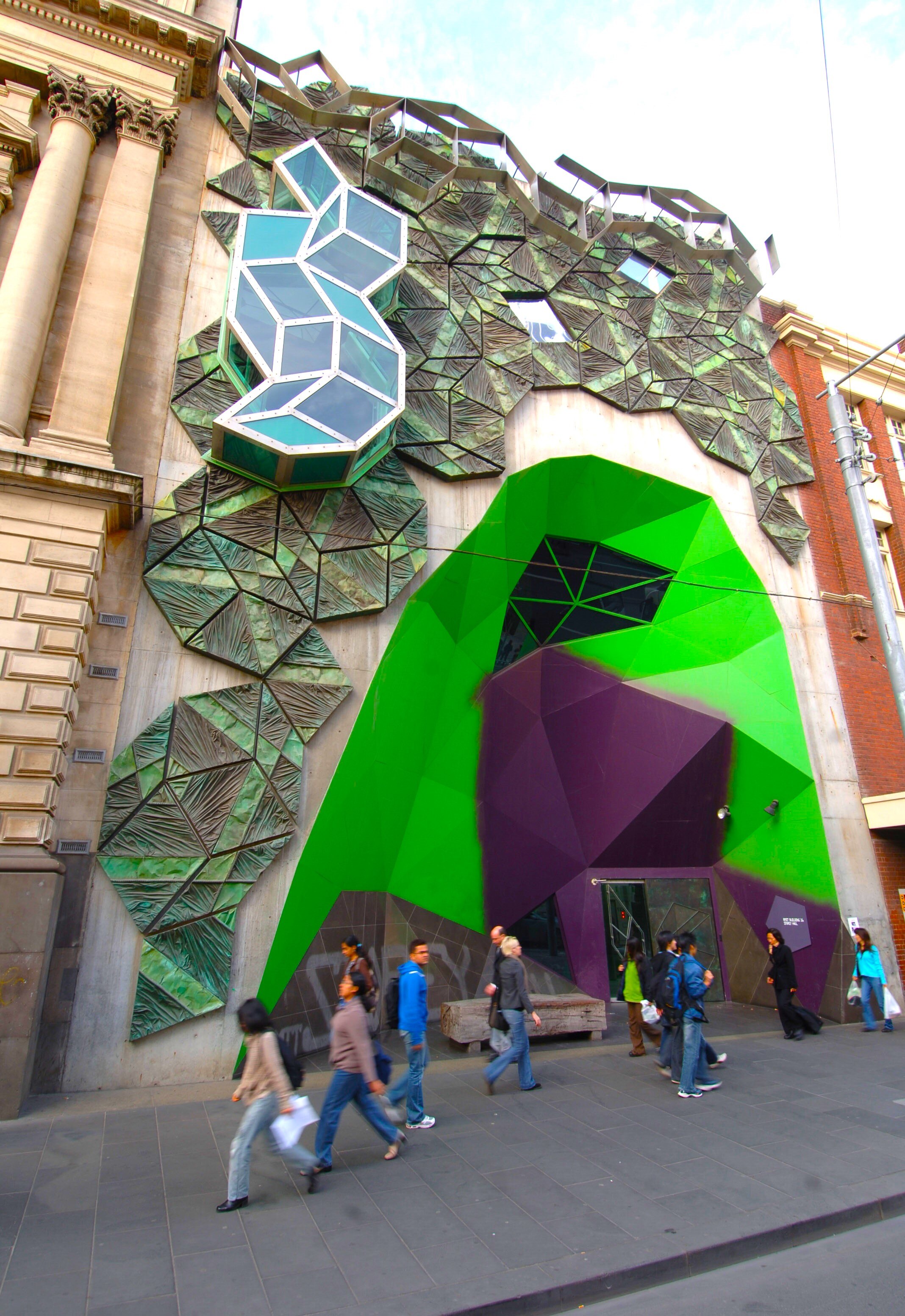 Сильное и красочное здание в центре города Мельбурн. У него геометрические формы и зеленая и фиолетовая арка над входом