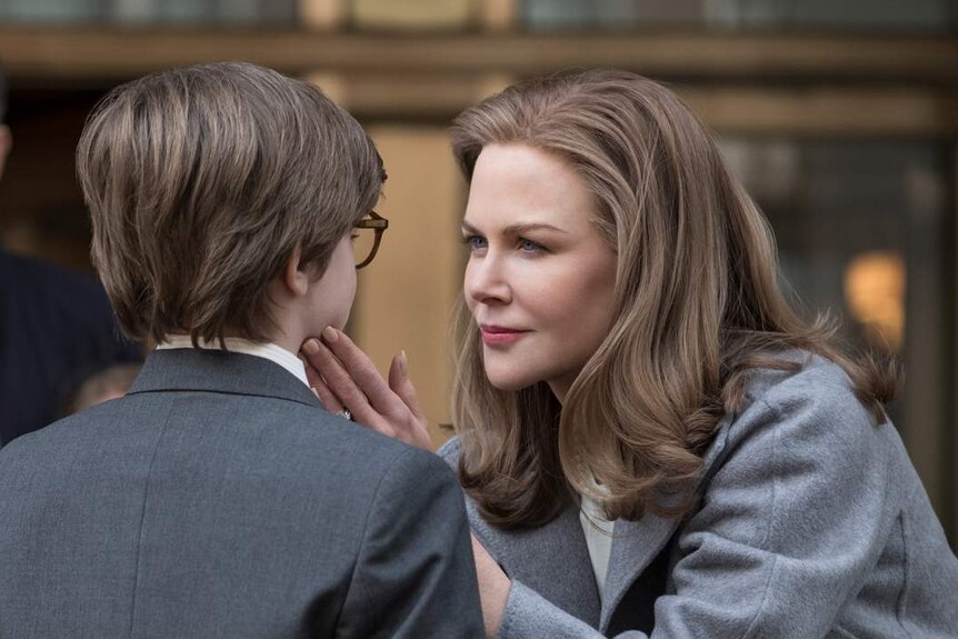 Nicole Kidman leaning down and looking in eyes of young boy who has back to camera, with her hand on his face.