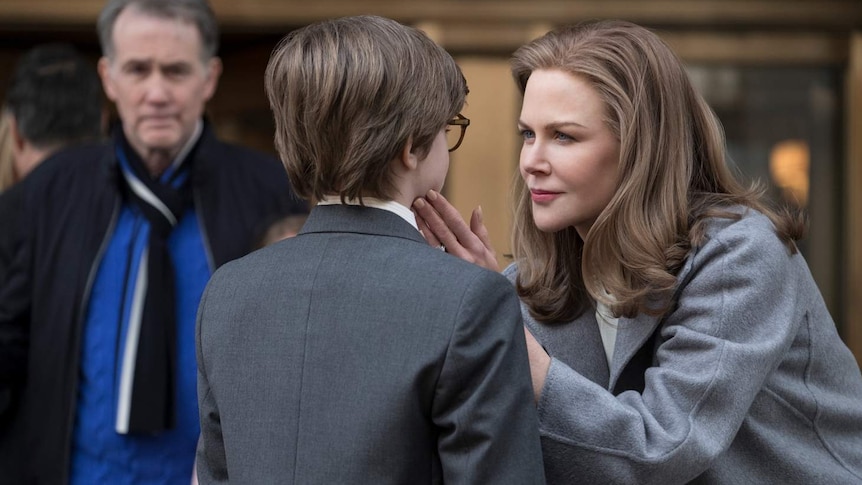Nicole Kidman leaning down and looking in eyes of young boy who has back to camera, with her hand on his face.