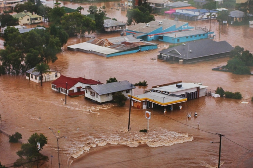 Houses submerged in red, muddy, fast-flowing water.