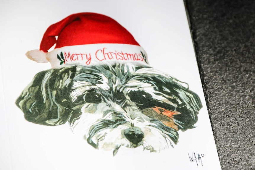 A drawing on a card of a puppy wearing a Christmas hat.