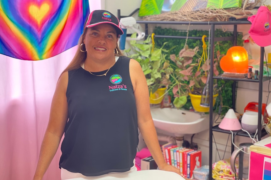 Women with matching shirt and cap stands in front of a rainbow flag with plants and treatments behind her  