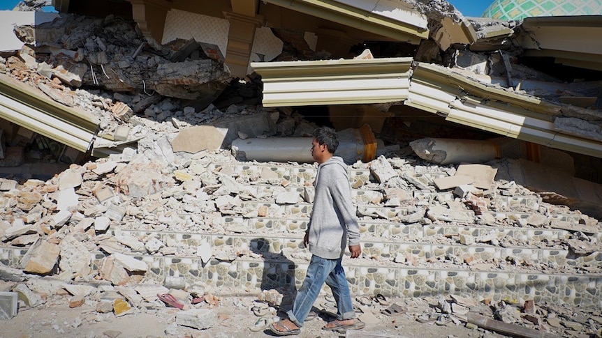 Lalu Fauzan walks beside the towering pile of rubble that used to be his village mosque.
