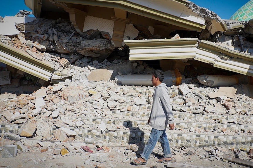 Lalu Fauzan walks beside the towering pile of rubble that used to be his village mosque.