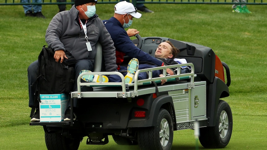 A man looks up while laying down on a stretcher on a cart.