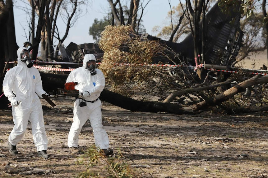 two people in white hazmat suit carrying wreckage