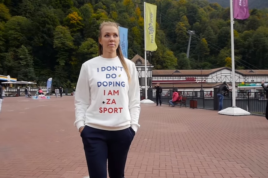 A woman wears a white jumper with 'I don't do doping' written on it while walking in public.