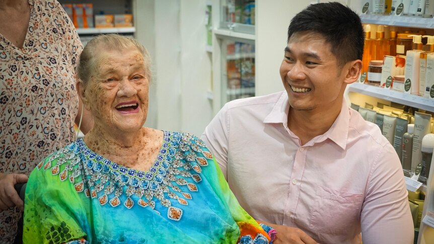 A young pharmacist laughs with an older lady customer.
