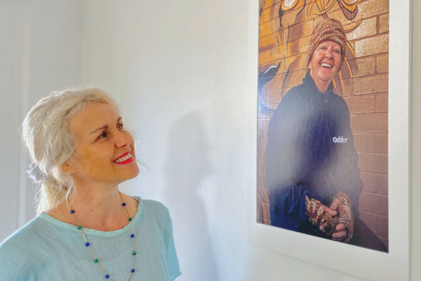 A smiling woman looks up at a photograph on the wall