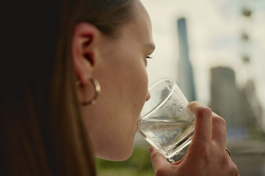 a close-up of a woman drinking a glass of water. she's wearing gold hoop earrings