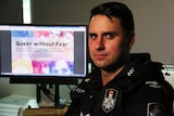 Senior Constable Ben Bjarnesen sits in his office in Brisbane with Queer without Fear sign on his computer screen.