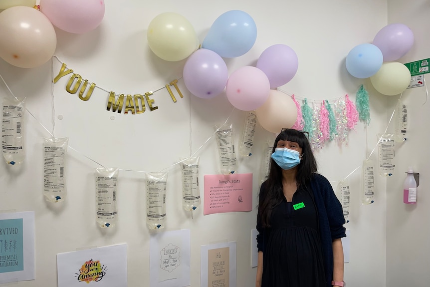 A woman standing in front of IV fluid bags and balloons.