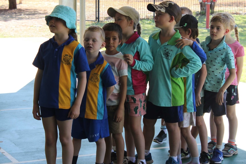Nine children in different uniforms line up in single file at a playground.
