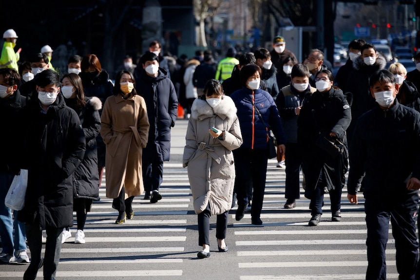 A crowd of people dressed warmly cross the road at a pedestrian crossing in South Korea. 