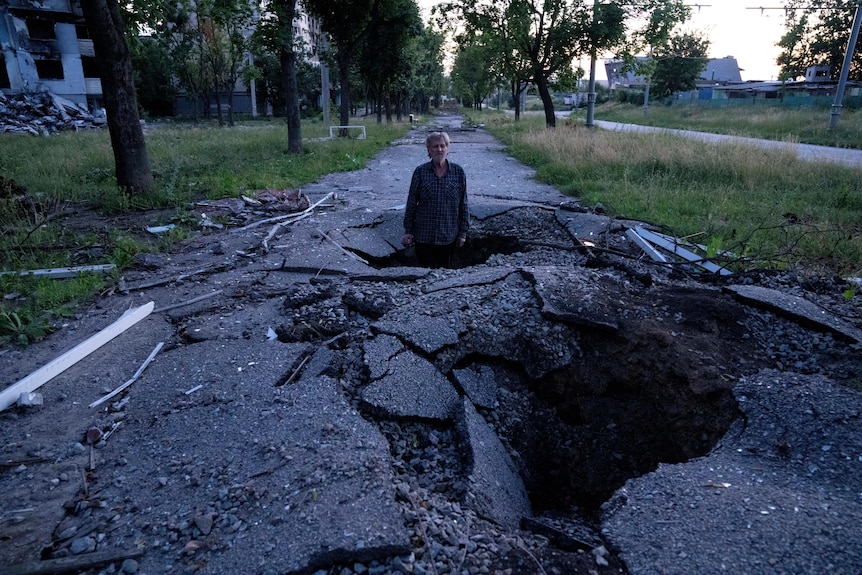 Viktor Shevchenko stands in a crater to show how deep it was that created by a shell after a Russian attack.