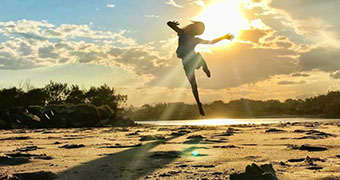 A person jumps for joy in the sunlight at the beach.