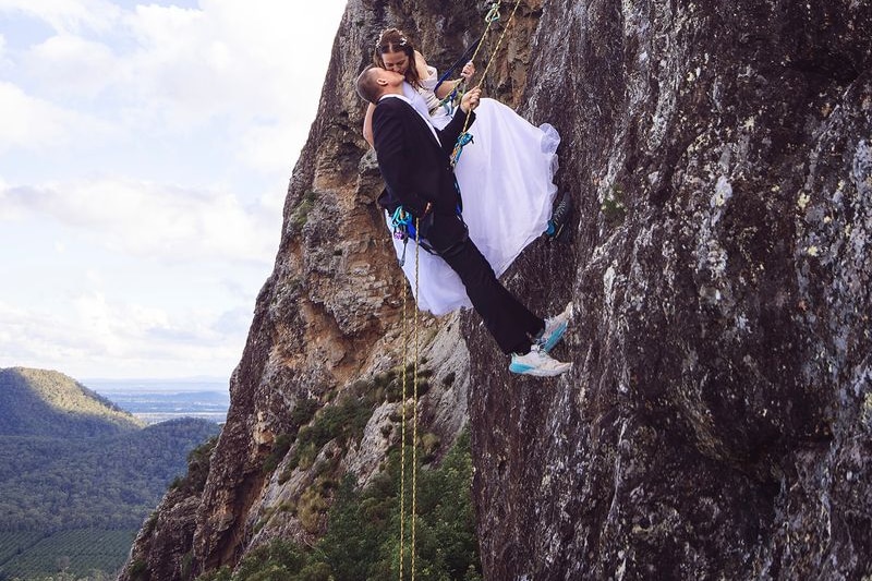 A couple fully dressed in wedding gear kiss while abseiling.