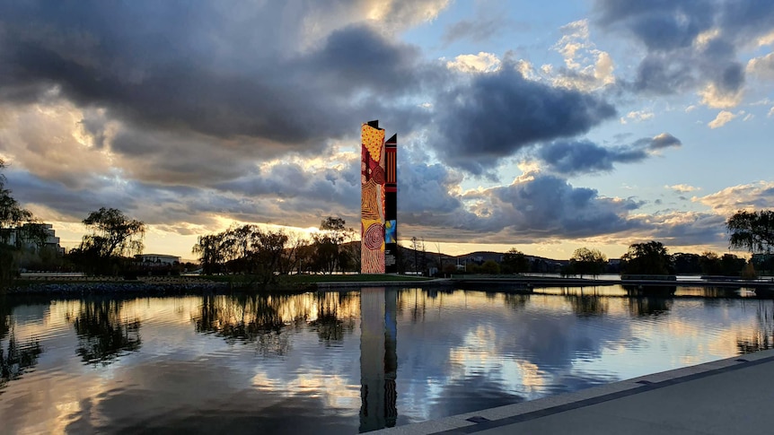 Tower covered in aboriginal art shot from across a still lake at a cloudy dawn or dusk
