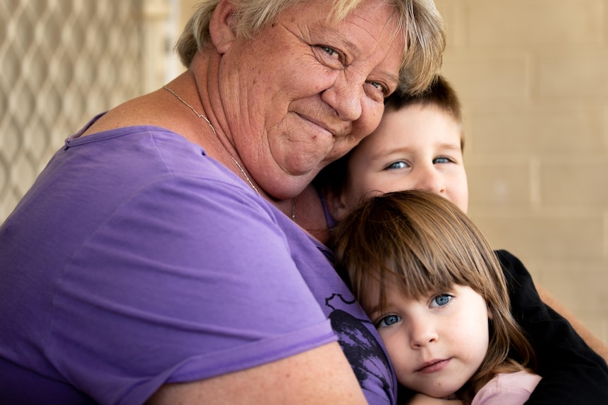 Une femme embrasse deux jeunes enfants, un garçon et une fille.