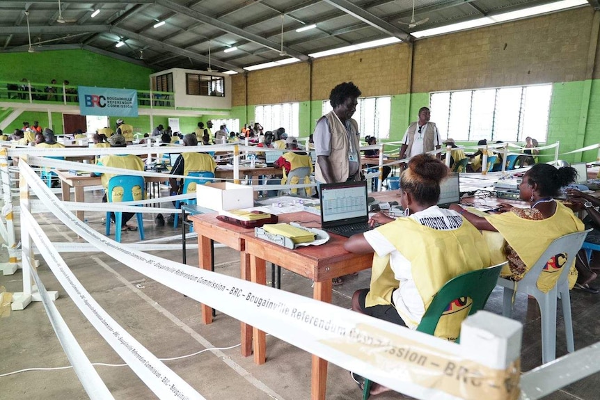 People sitting at desks in a factory-like room count votes from the Bougainville referendum.
