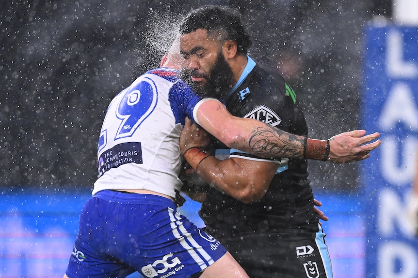 A Cronulla NRL player makes a hit-up with the ball as he is tackled by a Canterbury opponent.