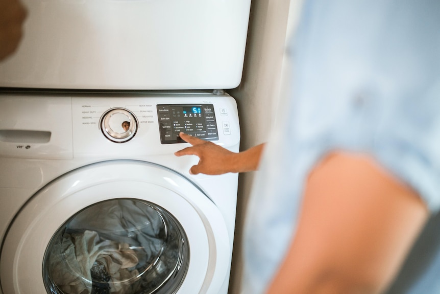 a man pushes the button on a washing machine that's full of clothes