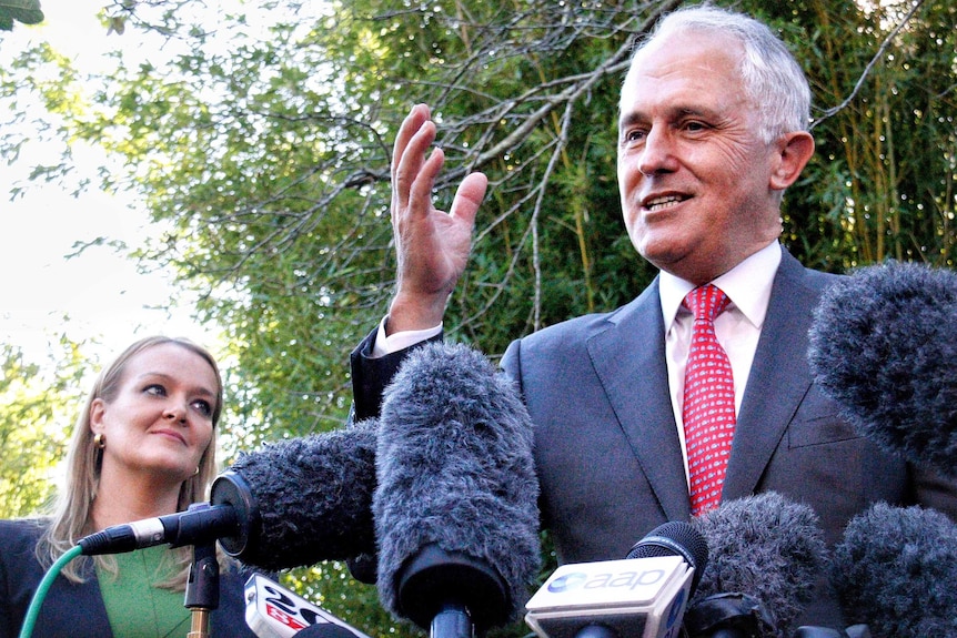 Low down view of Malcolm Turnbull speaking at a microphone as Fiona Scott looks on.