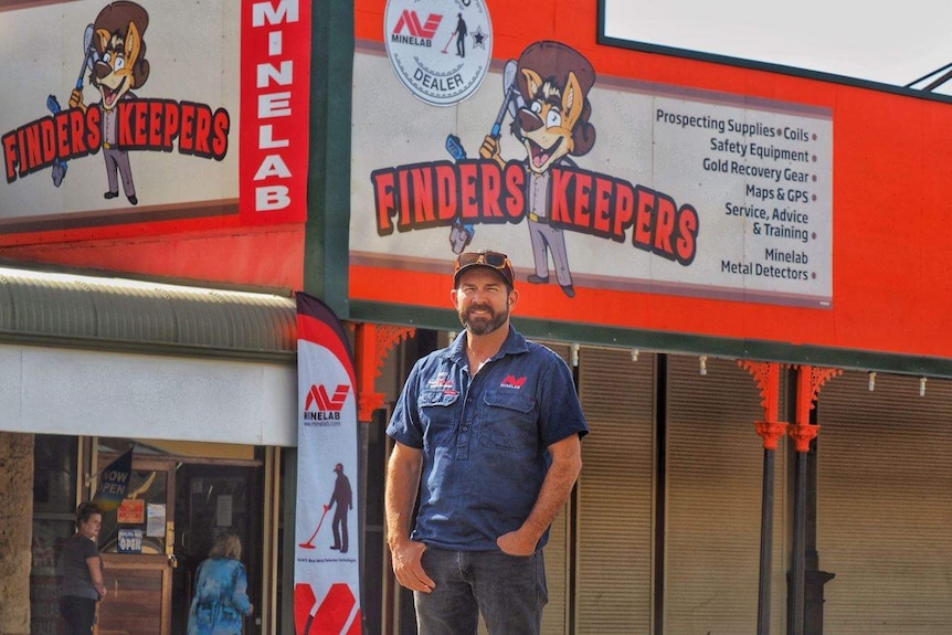 A man stands in front of a gold prospecting equipment store.