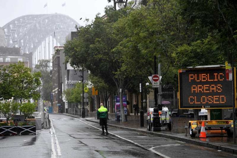 A man stands in an empty street before the Sydney Harbour Bridge.