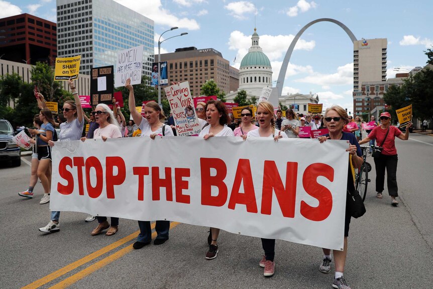 Women hold a large banner and march down a street in support of women's reproductive health choices