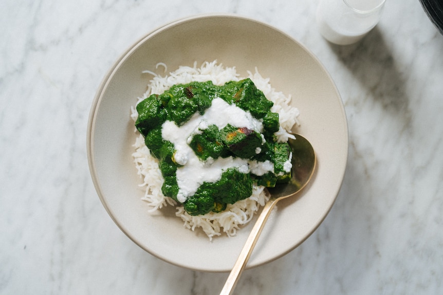 A bowl of white rice topped with spinach and chickpea curry