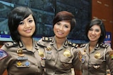 Three female police officers stand in front of a large screen wearing uniforms