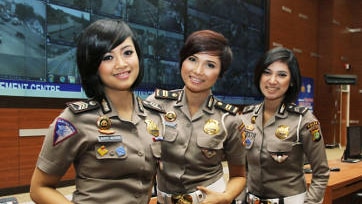 Three female police officers stand in front of a large screen wearing uniforms