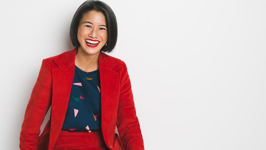 A portrait of a middle-aged woman with a big smile and red lipstick with brown short hair and a red suit. 