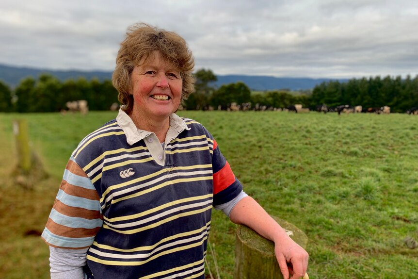 A woman standing in a paddock in front of cows smiles at the camera.