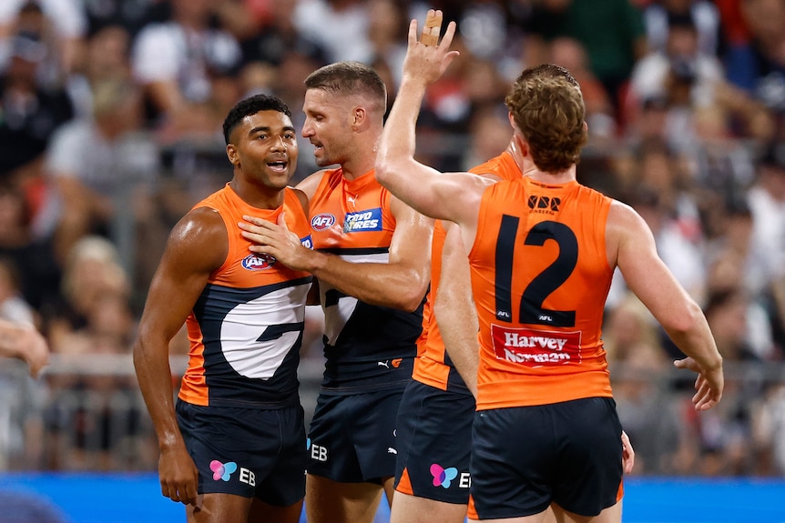 A group of GWS players gather to congratulate a teammate (on the left) who has kicked a goal.