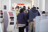 A crowd of passengers crowd around self check-in counters