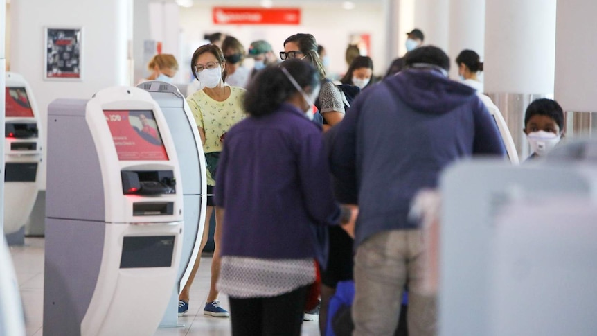 A crowd of passengers crowd around self check-in counters