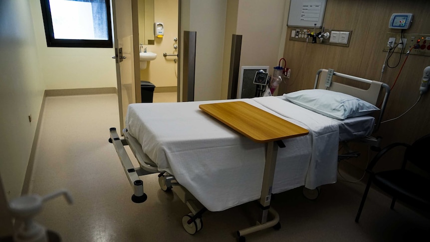 A photo of a small hospital room with a bathroom attached and a small window.