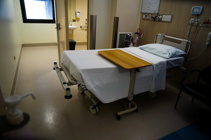 A photo of a small hospital room with a bathroom attached and a small window.