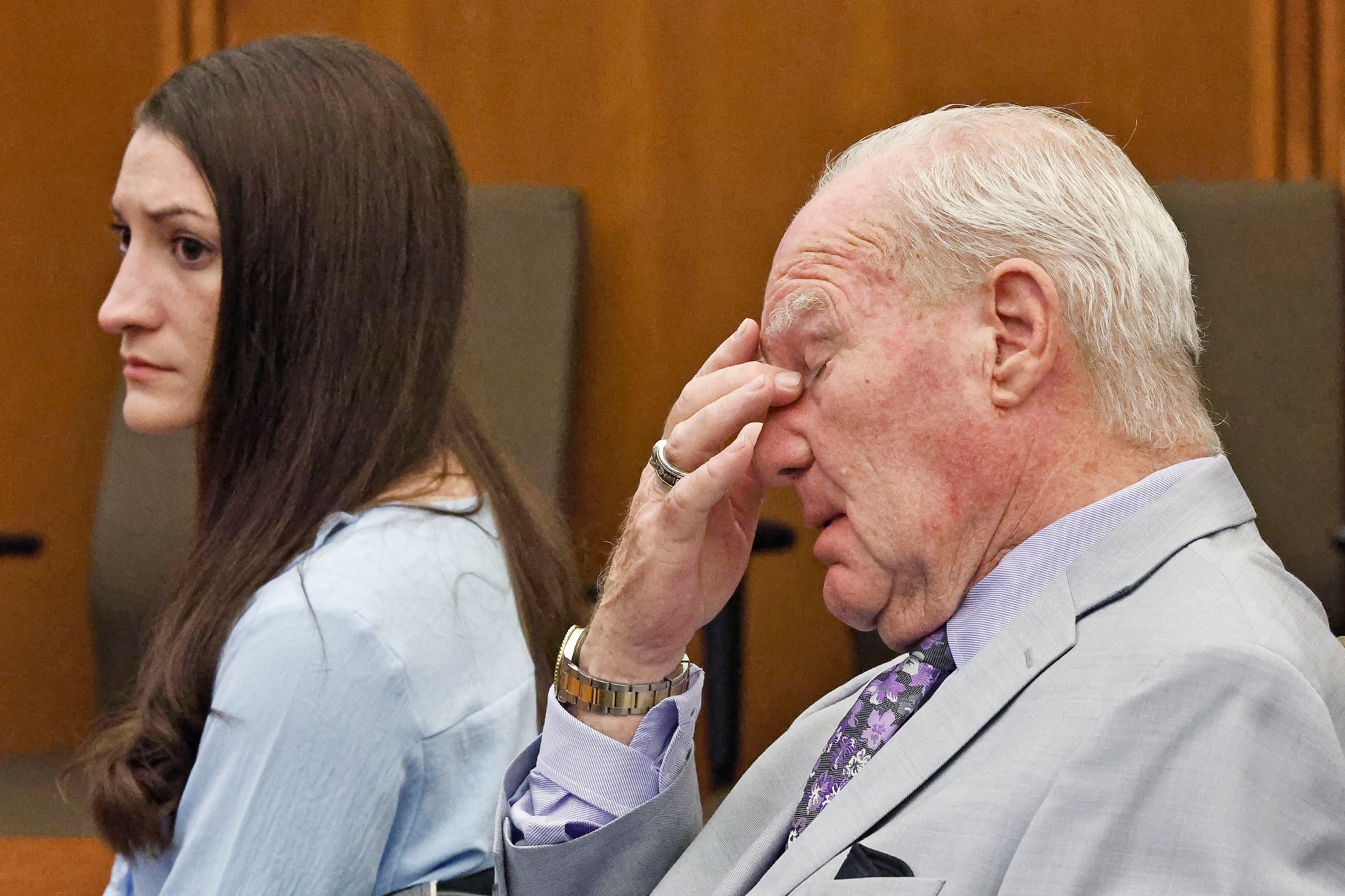 An older man pressing his hand to the bridge of his nose, sitting beside a brunette woman