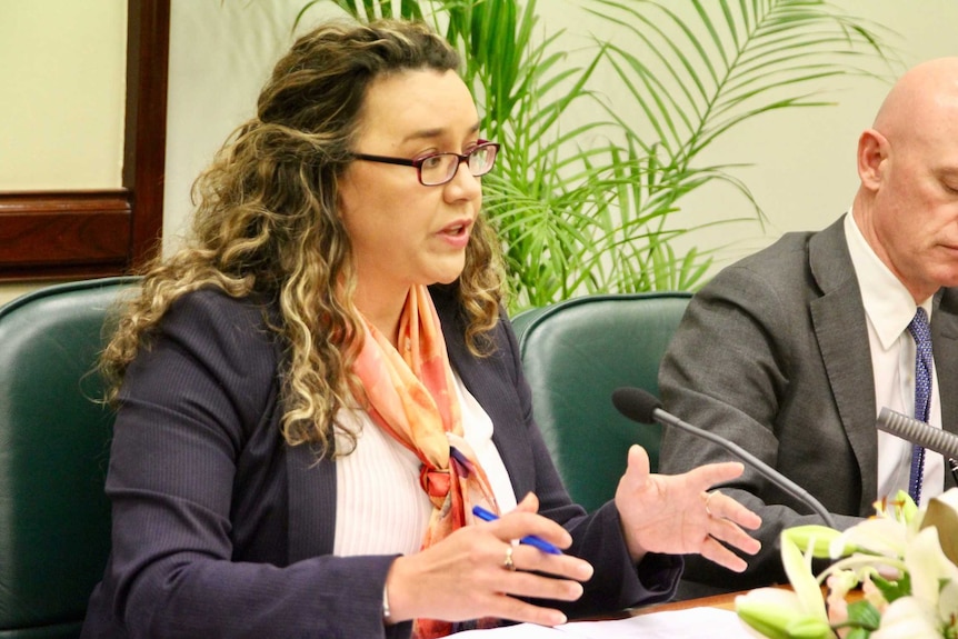 A woman and a man in suits sit at a boardroom table.