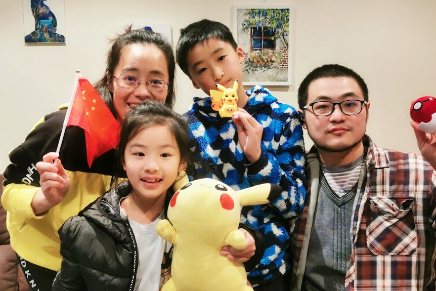 Un couple et leurs deux enfants posent avec des figurines Pokémon et un drapeau chinois