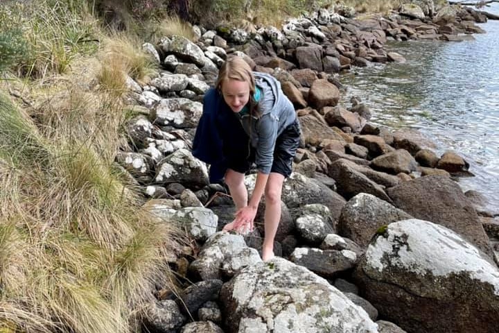 A woman walking across a rocky shoreline